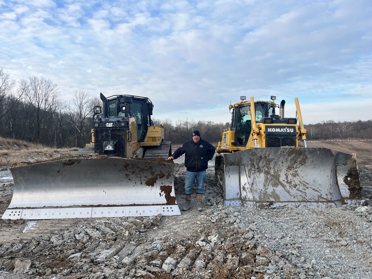 man standing in between two parked bulldozers